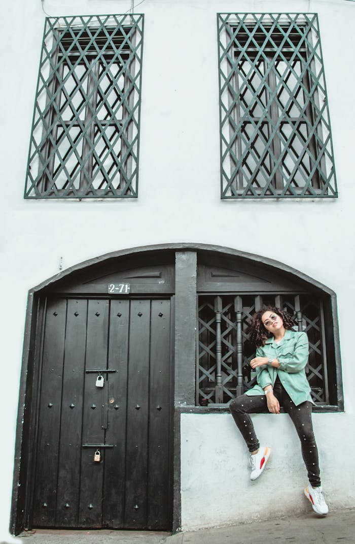 Woman posing outside a modern urban building with lattice windows and arched doorway.